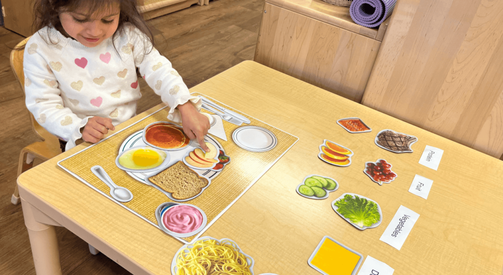 Young child engaging in a Montessori food activity, arranging picture cards of healthy foods into food groups on a placemat.